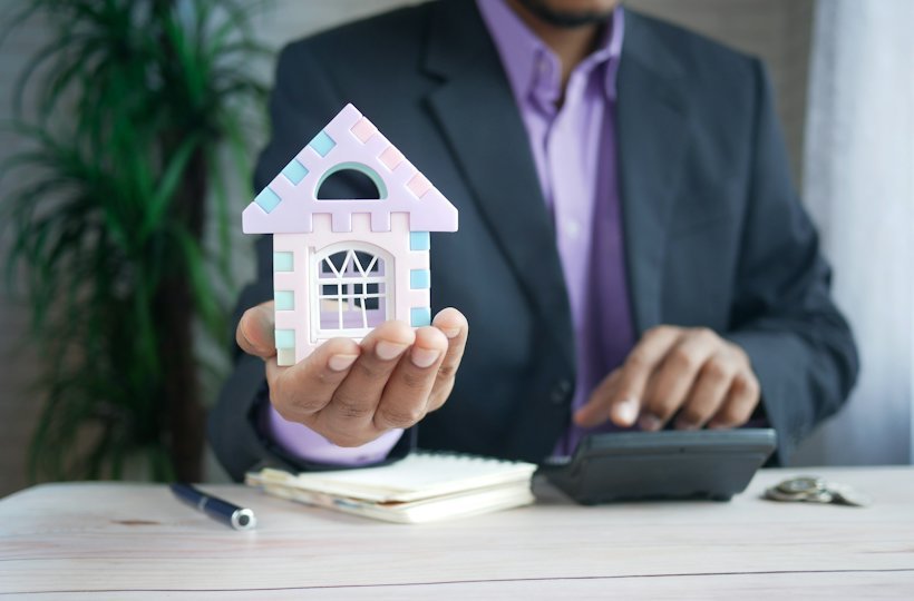 Hands holding a model house beside a calculator on a desk